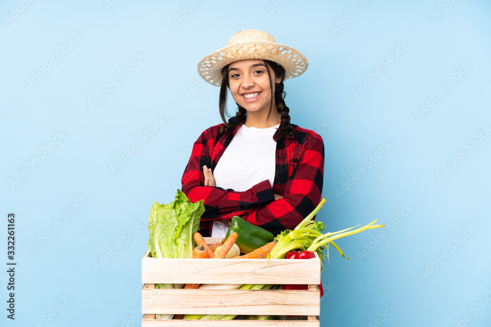 Young farmer Woman holding fresh vegetables in a wooden basket keeping the arms crossed in frontal position