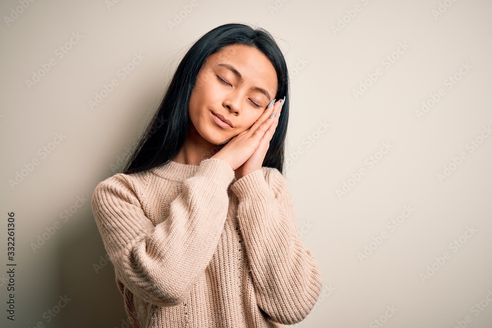 Young beautiful chinese woman wearing casual sweater over isolated white background sleeping tired dreaming and posing with hands together while smiling with closed eyes. Young beautiful chinese woman wearing casual sweater over isolated white background sleeping tired dreaming and posing with hands together while smiling with closed eyes.