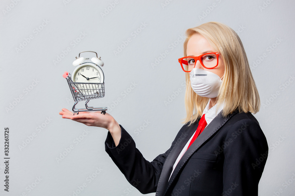 Businesswoman in face mask and red glasses holds alarm clock and cart Businesswoman in face mask and red glasses holds alarm clock and cart