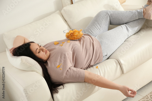 Lazy overweight woman with chips resting on sofa at home