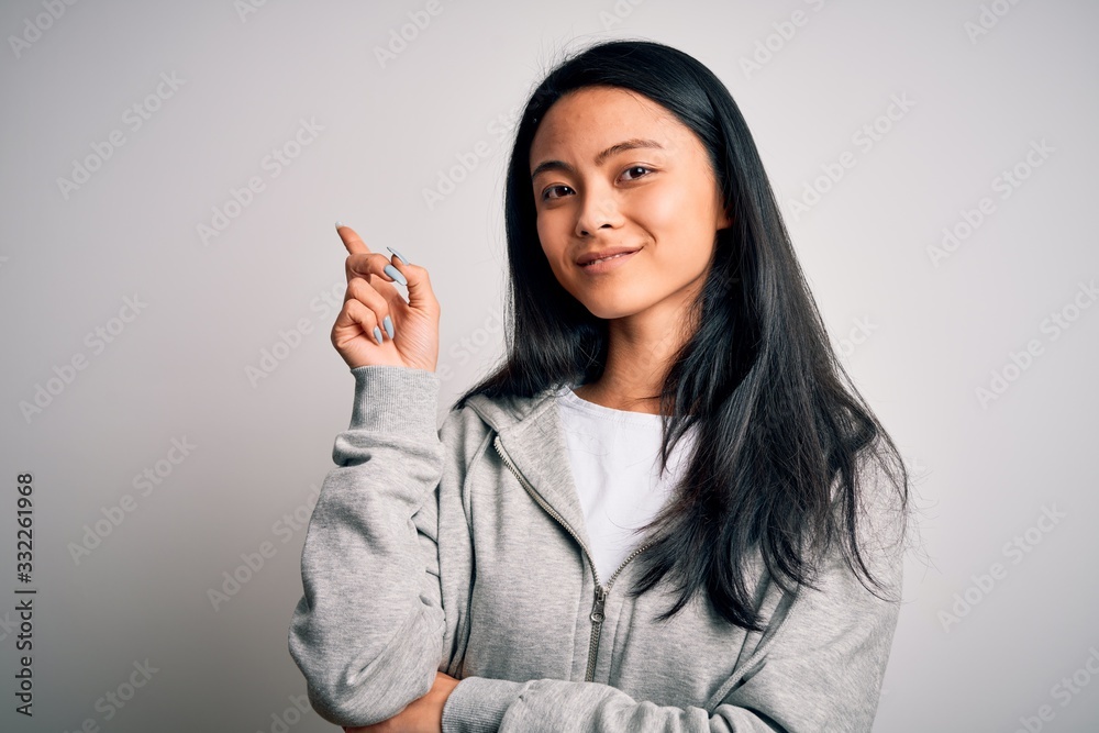 Young beautiful chinese sporty woman wearing sweatshirt over isolated white background with a big smile on face, pointing with hand and finger to the side looking at the camera. Young beautiful chinese sporty woman wearing sweatshirt over isolated white background with a big smile on face, pointing with hand and finger to the side looking at the camera.