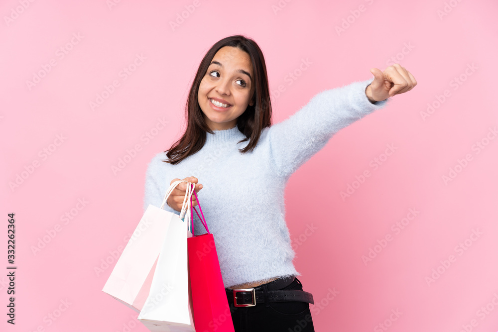 Young woman with shopping bag over isolated pink background giving a thumbs up gesture