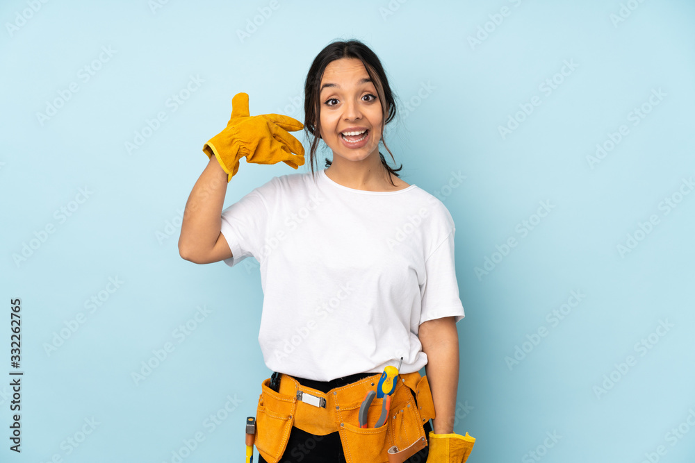 Young electrician woman isolated on blue background making phone gesture. Call me back sign Young electrician woman isolated on blue background making phone gesture. Call me back sign