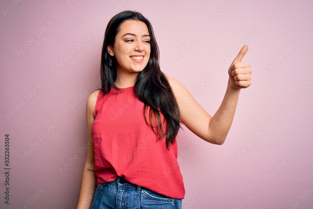 Young brunette woman wearing casual summer shirt over pink isolated background Looking proud, smiling doing thumbs up gesture to the side Young brunette woman wearing casual summer shirt over pink isolated background Looking proud, smiling doing thumbs up gesture to the side