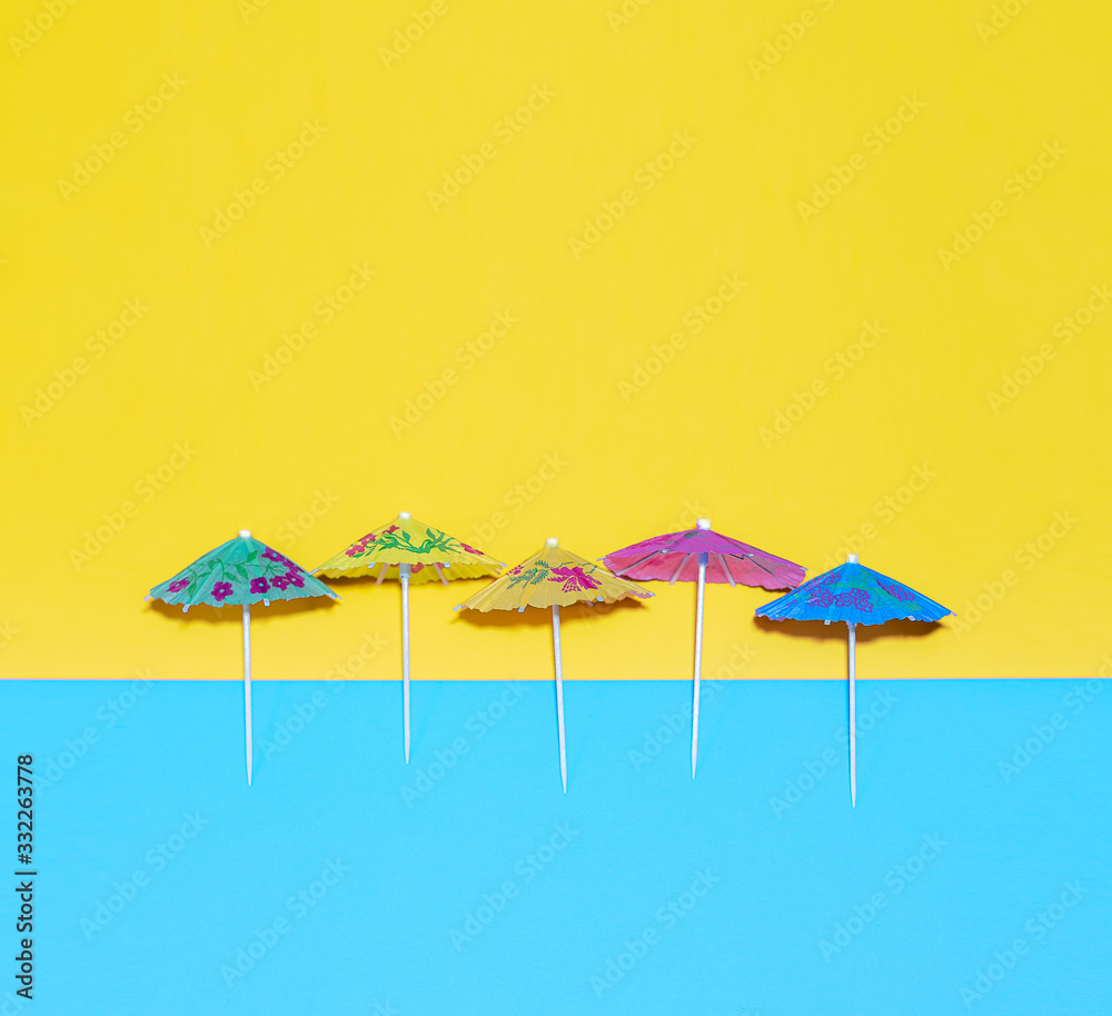 Summer concept with colorfull paper cocktail umbrella’s against a blue and yellow background flat layer with space for copy
