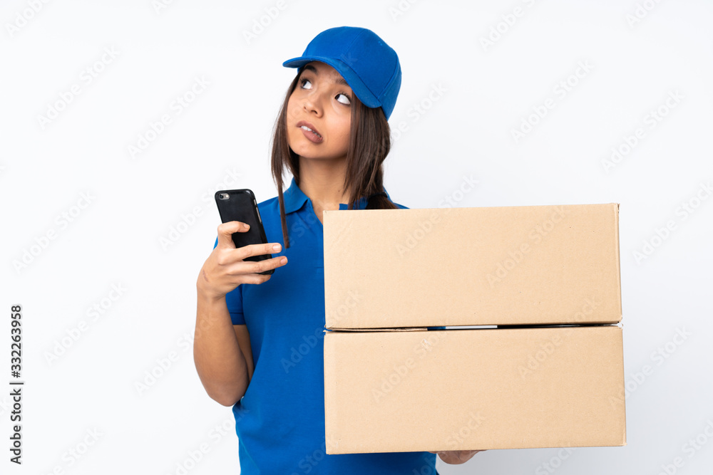 Young delivery brunette girl over isolated white background holding coffee to take away and a mobile while thinking something Young delivery brunette girl over isolated white background holding coffee to take away and a mobile while thinking something