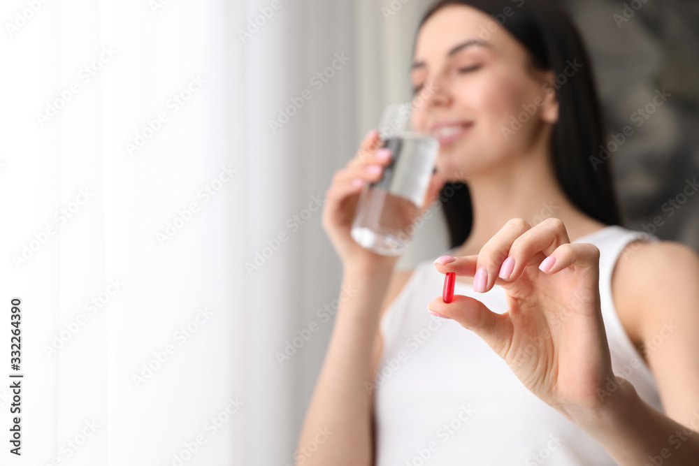 Woman with vitamin capsule and glass of water indoors, focus on hand. Space for text Woman with vitamin capsule and glass of water indoors, focus on hand. Space for text