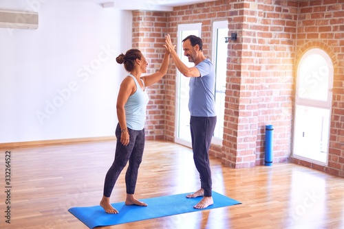 Middle age beautiful sporty couple smiling happy. Standing with smile on face highing five at gym