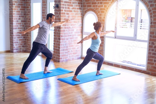 Middle age beautiful sporty couple smiling happy. Standing with smile on face practicing yoga doing warrior pose at gym