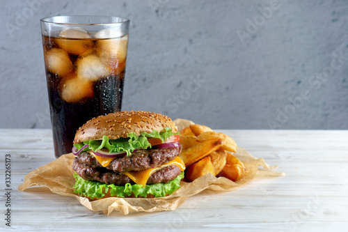 Burger with two beef patties and cheese, with a glass of Cola on a light background