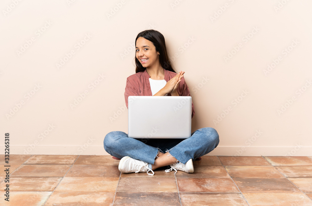 Young mixed race woman with a laptop sitting on the floor applauding Young mixed race woman with a laptop sitting on the floor applauding