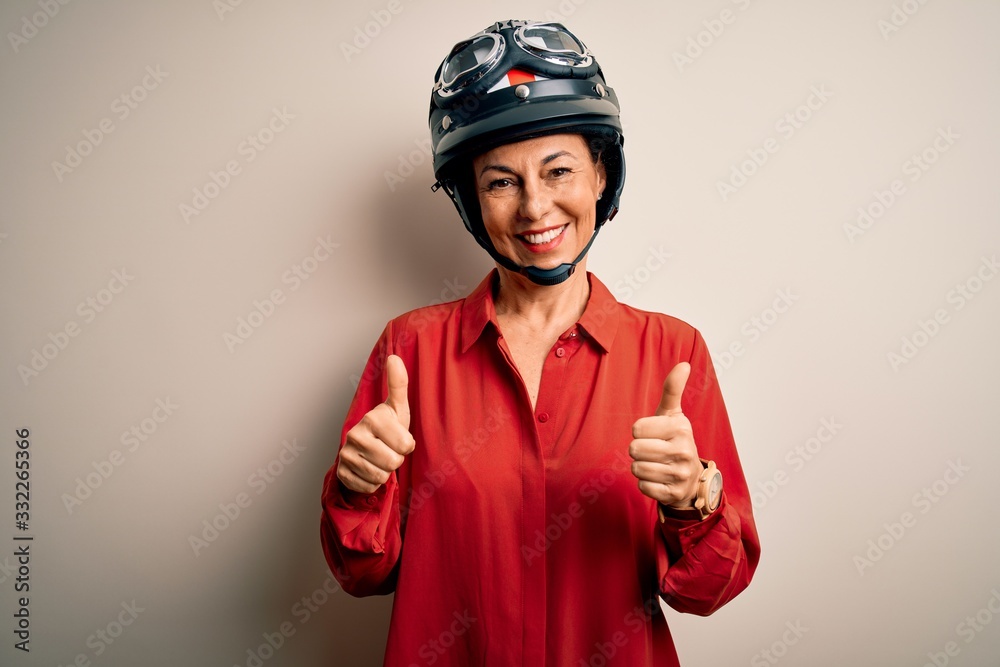 Middle age motorcyclist woman wearing motorcycle helmet over isolated white background success sign doing positive gesture with hand, thumbs up smiling and happy. Cheerful expression and winner