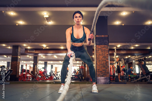 Caucasian fit woman dressed in sportsoutfit posing with battle ropes at gym.