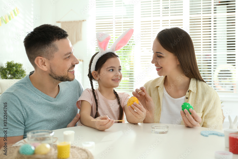 Happy father, mother and daughter painting Easter eggs at table indoors Happy father, mother and daughter painting Easter eggs at table indoors