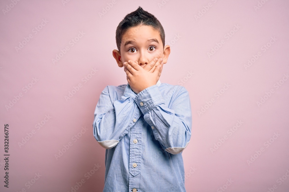 Young little boy kid wearing elegant shirt standing over pink isolated background shocked covering mouth with hands for mistake. Secret concept.