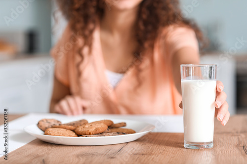 Young African-American woman taking glass of milk from kitchen table