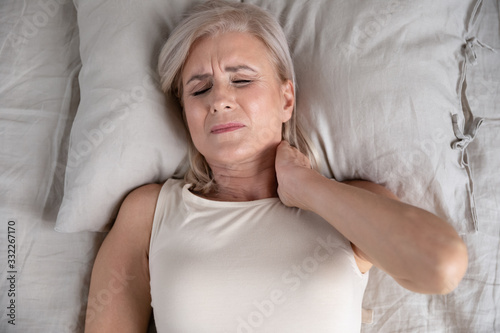 Canvas Print Top above view head shot close up older unhappy woman lying in bed, waking up in morning, feeling strong neck ache