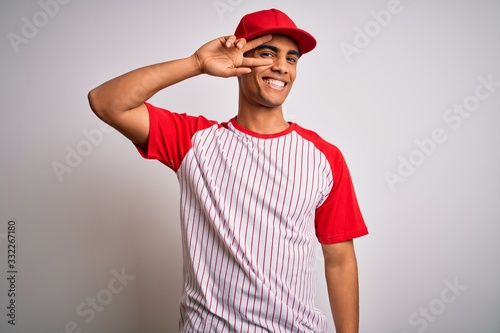 Young handsome african american sportsman wearing striped baseball t-shirt and cap Doing peace symbol with fingers over face  smiling cheerful showing victory