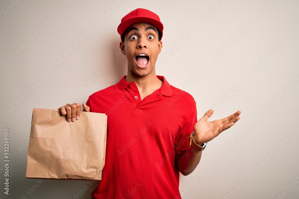Young handsome african american delivery man holding paper bag with takeaway food very happy and excited, winner expression celebrating victory screaming with big smile and raised hands Young handsome african american delivery man holding paper bag with takeaway food very happy and excited, winner expression celebrating victory screaming with big smile and raised hands