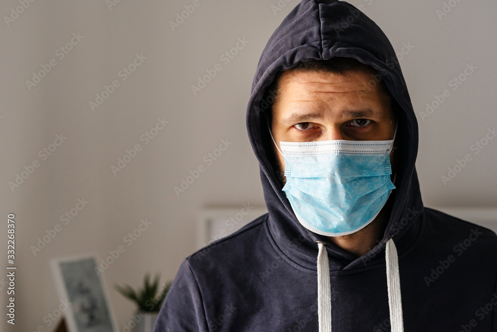 Portrait of caucasian adult man wearing protective medical mask and hood on his head to protect from virus bacteria pandemic pollution looking to the camera in day front view at home Portrait of caucasian adult man wearing protective medical mask and hood on his head to protect from virus bacteria pandemic pollution looking to the camera in day front view at home
