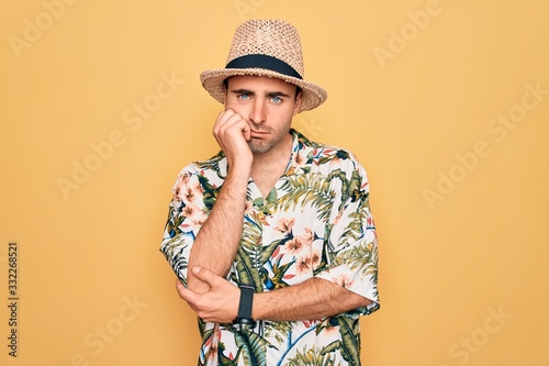 Young handsome man with blue eyes on vacation wearing summer florar shirt and hat thinking looking tired and bored with depression problems with crossed arms.
