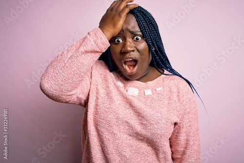 African american plus size woman with braids wearing casual sweater over pink background surprised with hand on head for mistake, remember error. Forgot, bad memory concept. © Krakenimages.com