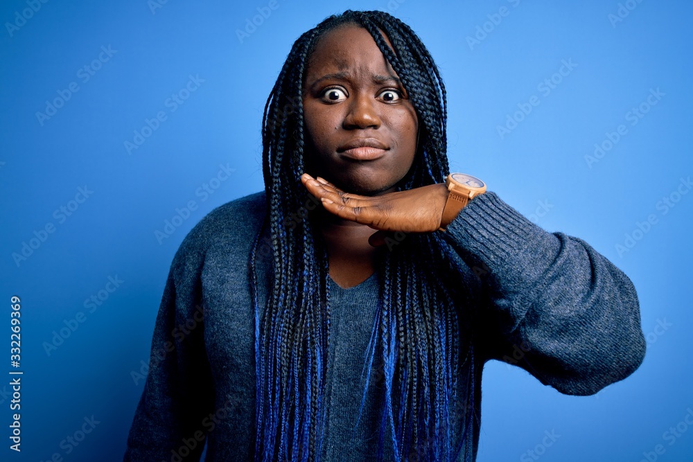 African american plus size woman with braids wearing casual sweater over blue background cutting throat with hand as knife, threaten aggression with furious violence African american plus size woman with braids wearing casual sweater over blue background cutting throat with hand as knife, threaten aggression with furious violence