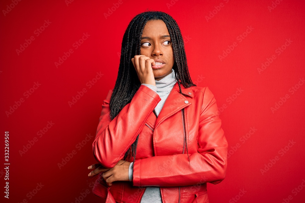 Young african american woman wearing cool fashion leather jacket over red isolated background looking stressed and nervous with hands on mouth biting nails. Anxiety problem.