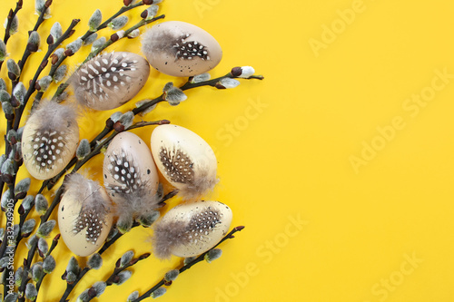 Easter eggs decorated with feathers next to Easter catkins on a yellow background photo