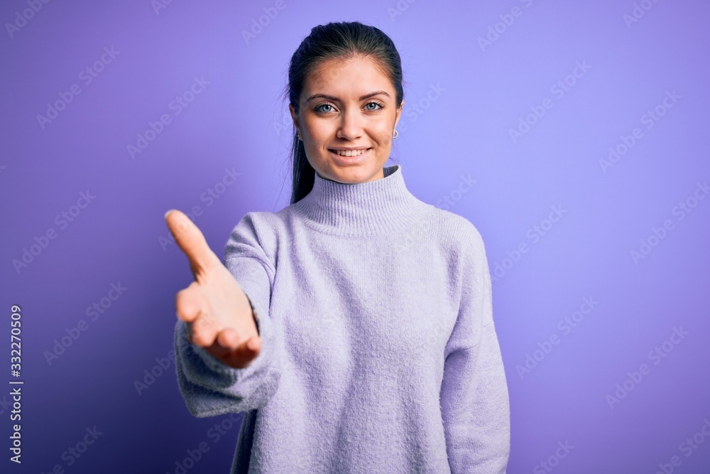 Young beautiful woman with blue eyes wearing casual turtleneck sweater over pink background smiling friendly offering handshake as greeting and welcoming. Successful business. Young beautiful woman with blue eyes wearing casual turtleneck sweater over pink background smiling friendly offering handshake as greeting and welcoming. Successful business.