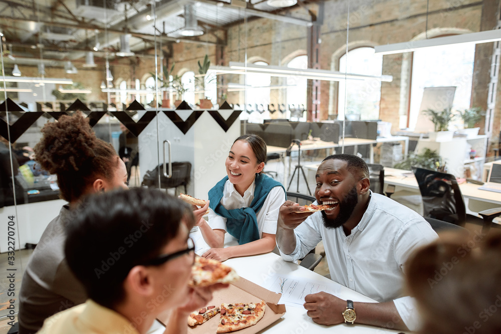 Time for pizza. Happy multicultural team eating pizza and smiling while having lunch in the modern office Time for pizza. Happy multicultural team eating pizza and smiling while having lunch in the modern office