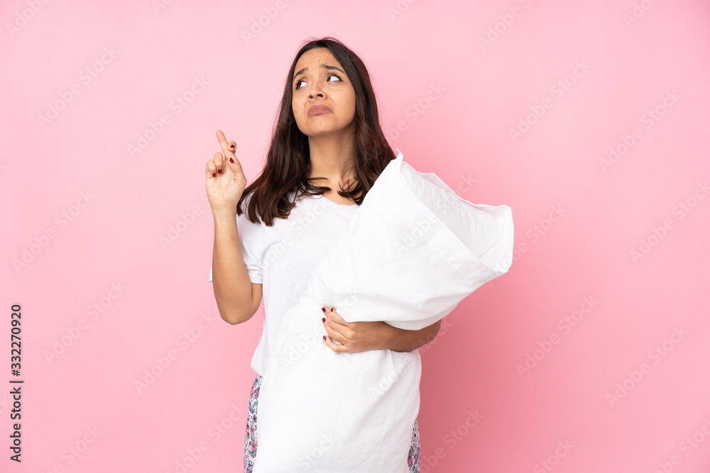 Young woman in pajamas isolated on pink background with fingers crossing and wishing the best Young woman in pajamas isolated on pink background with fingers crossing and wishing the best
