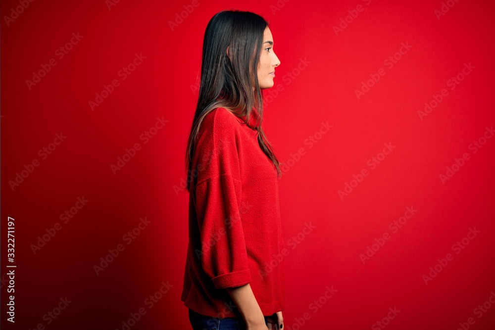 Young beautiful brunette woman wearing casual sweater over isolated red background looking to side, relax profile pose with natural face and confident smile. Young beautiful brunette woman wearing casual sweater over isolated red background looking to side, relax profile pose with natural face and confident smile.