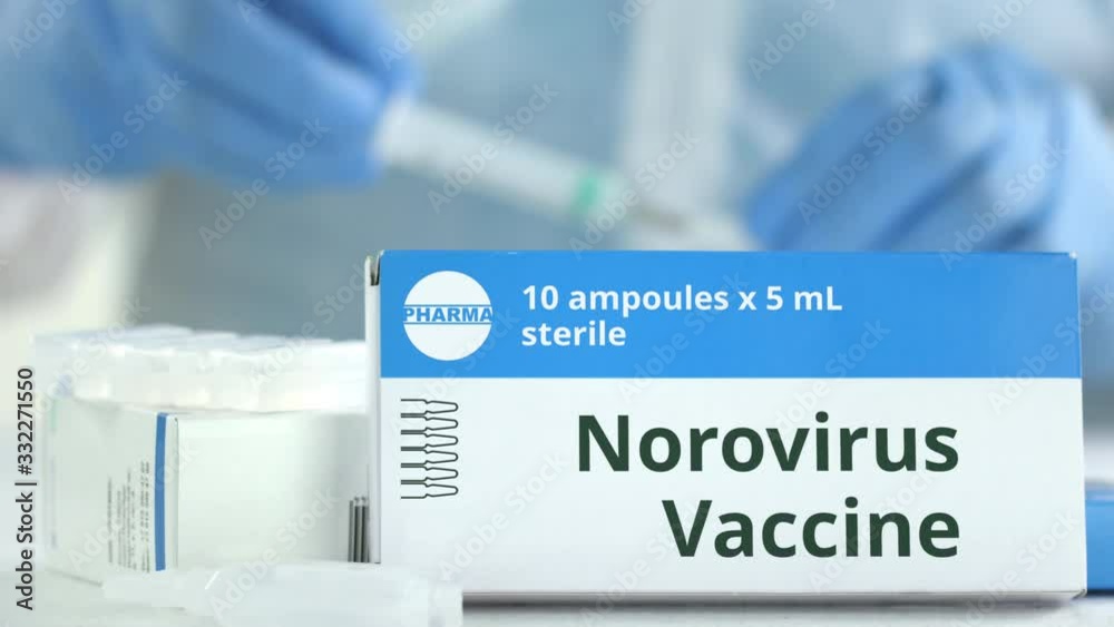 Ampoules with norovirus vaccine on the table near working laboratory assistant, fictional logo on the box Ampoules with norovirus vaccine on the table near working laboratory assistant, fictional logo on the box