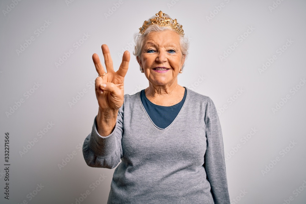 Senior beautiful grey-haired woman wearing golden queen crown over white background showing and pointing up with fingers number three while smiling confident and happy. Senior beautiful grey-haired woman wearing golden queen crown over white background showing and pointing up with fingers number three while smiling confident and happy.