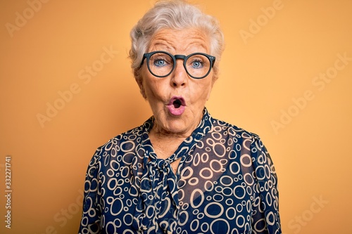 Senior beautiful grey-haired woman wearing casual shirt and glasses over yellow background afraid and shocked with surprise expression, fear and excited face.