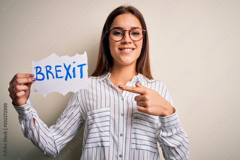 Young beautiful brunette woman holding paper with brexit message over white background very happy pointing with hand and finger Young beautiful brunette woman holding paper with brexit message over white background very happy pointing with hand and finger