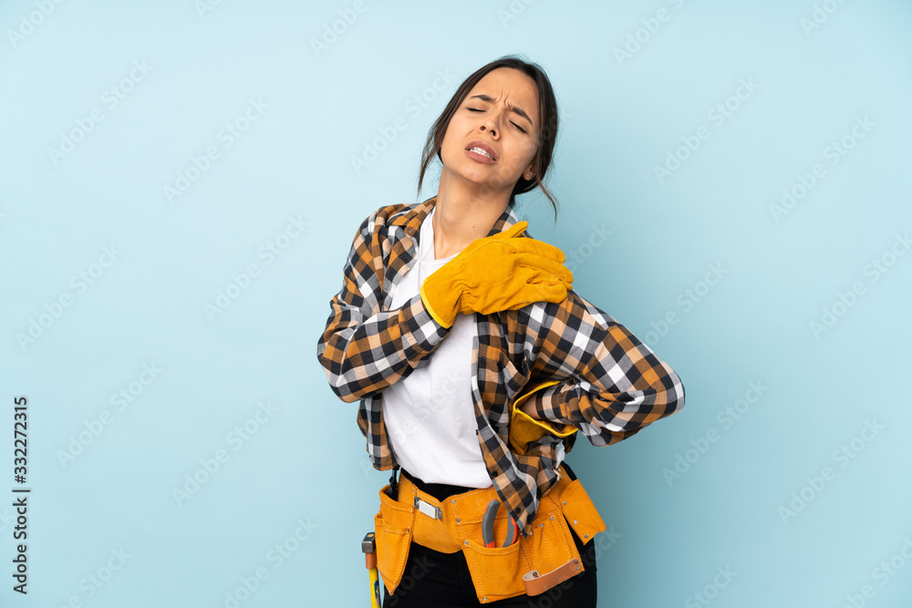 Young electrician woman isolated on blue background suffering from pain in shoulder for having made an effort Young electrician woman isolated on blue background suffering from pain in shoulder for having made an effort