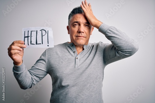 Middle age handsome grey-haired man holding paper with help message stressed with hand on head, shocked with shame and surprise face, angry and frustrated. Fear and upset for mistake. © Krakenimages.com