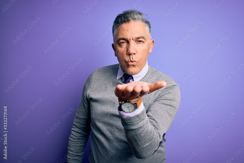 Middle age handsome grey-haired man wearing elegant sweater over purple background looking at the camera blowing a kiss with hand on air being lovely and sexy. Love expression. Middle age handsome grey-haired man wearing elegant sweater over purple background looking at the camera blowing a kiss with hand on air being lovely and sexy. Love expression.