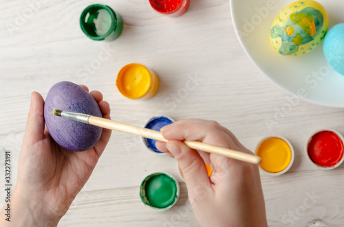 Child is painting egg in different color for Easter holiday, face is not visible
