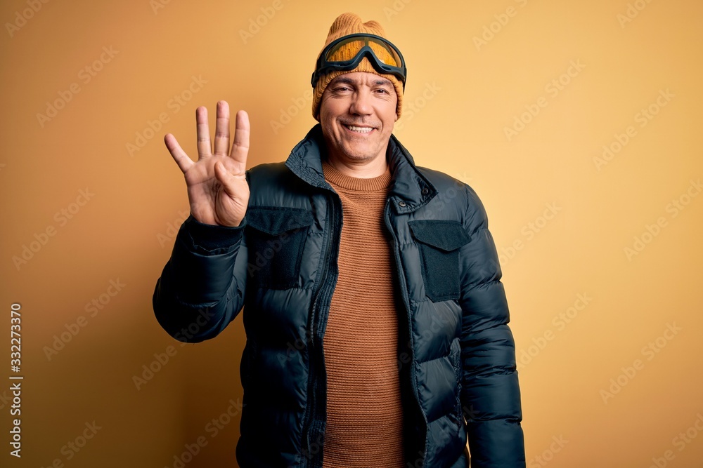 Middle age handsome grey-haired skier man on vacation wearing ski goggles showing and pointing up with fingers number four while smiling confident and happy. Middle age handsome grey-haired skier man on vacation wearing ski goggles showing and pointing up with fingers number four while smiling confident and happy.