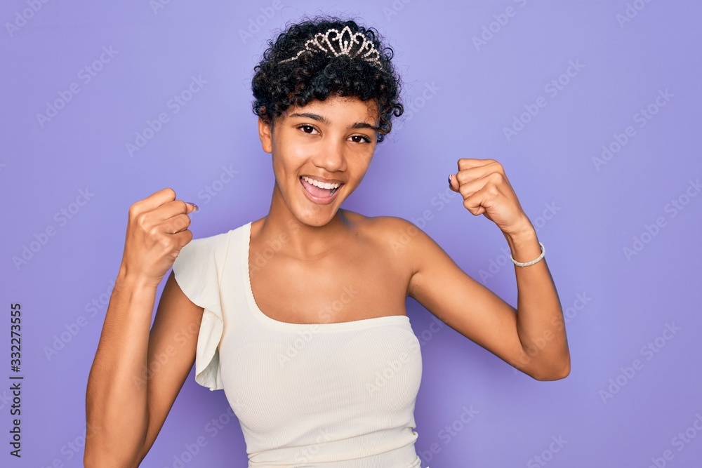 Young beautiful african american afro woman wearing tiara crown over purple background celebrating surprised and amazed for success with arms raised and open eyes. Winner concept. Young beautiful african american afro woman wearing tiara crown over purple background celebrating surprised and amazed for success with arms raised and open eyes. Winner concept.