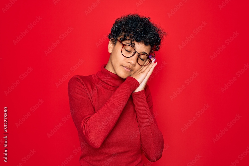 Young beautiful african american afro woman wearing turtleneck sweater and glasses sleeping tired dreaming and posing with hands together while smiling with closed eyes. Young beautiful african american afro woman wearing turtleneck sweater and glasses sleeping tired dreaming and posing with hands together while smiling with closed eyes.