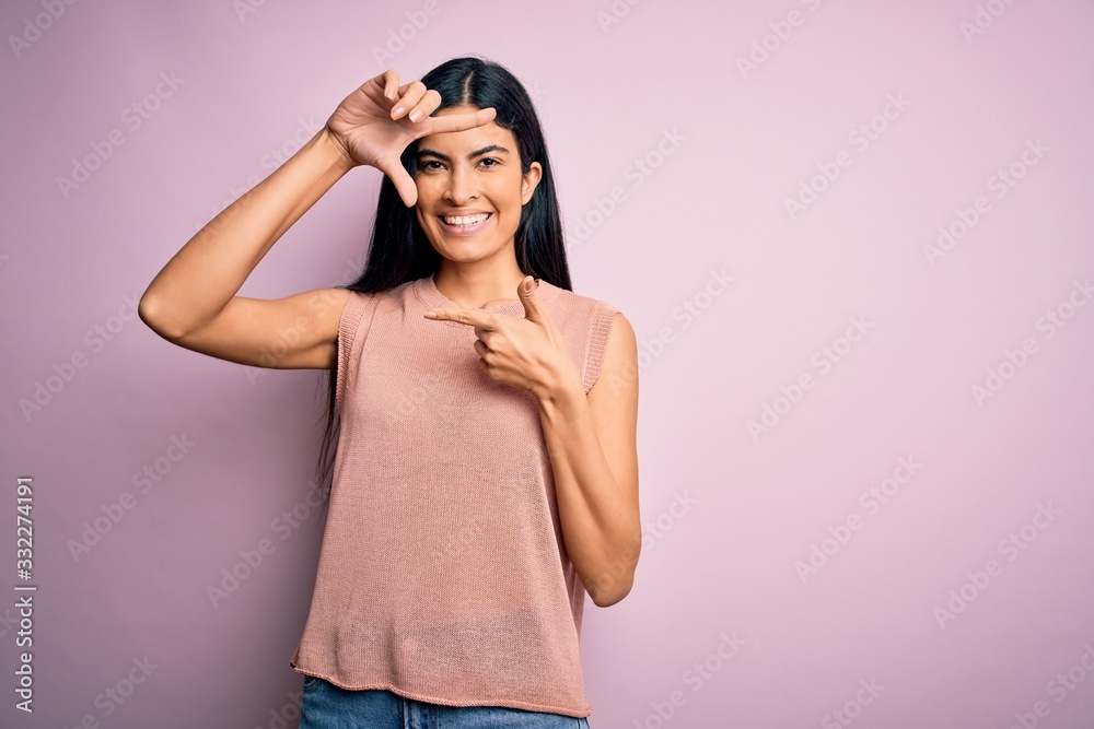 Fototapeta premium Young beautiful hispanic fashion woman wearing casual sweater over pink background smiling making frame with hands and fingers with happy face. Creativity and photography concept.