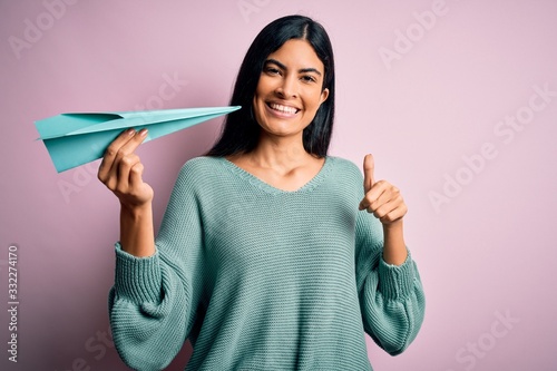 Foto Young beautiful hispanic woman holding paper plane and communication and travel