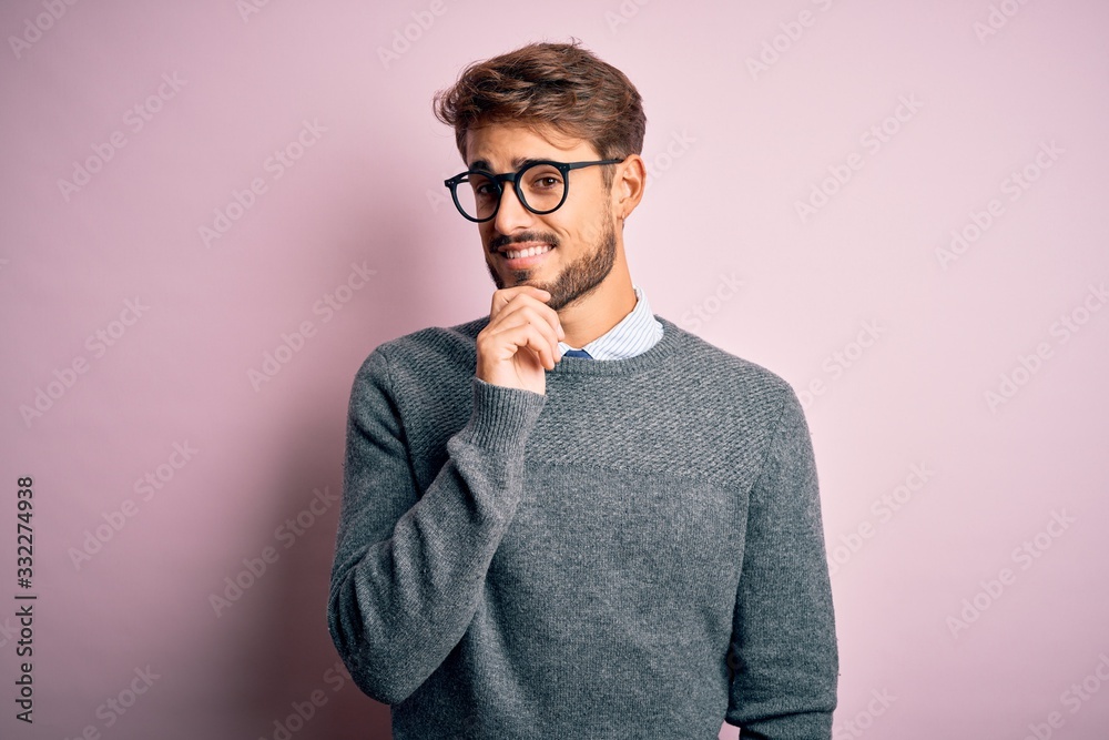 Young handsome man with beard wearing glasses and sweater standing over pink background looking confident at the camera with smile with crossed arms and hand raised on chin. Thinking positive. Young handsome man with beard wearing glasses and sweater standing over pink background looking confident at the camera with smile with crossed arms and hand raised on chin. Thinking positive.