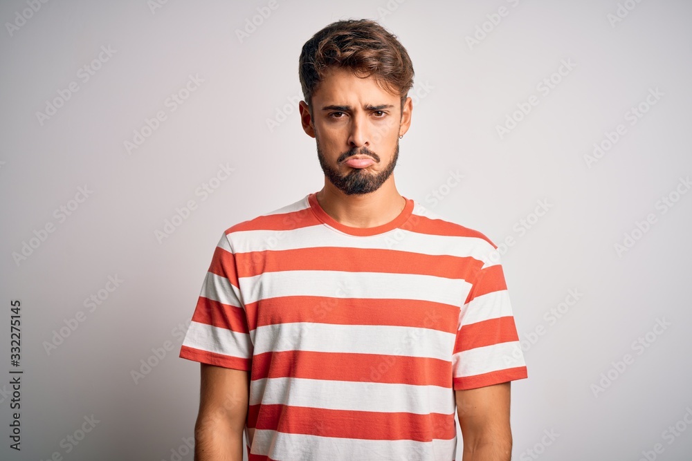 Obraz premium Young handsome man with beard wearing striped t-shirt standing over white background depressed and worry for distress, crying angry and afraid. Sad expression.