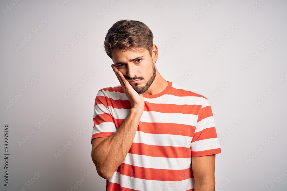 Young handsome man with beard wearing striped t-shirt standing over white background thinking looking tired and bored with depression problems with crossed arms. Young handsome man with beard wearing striped t-shirt standing over white background thinking looking tired and bored with depression problems with crossed arms.