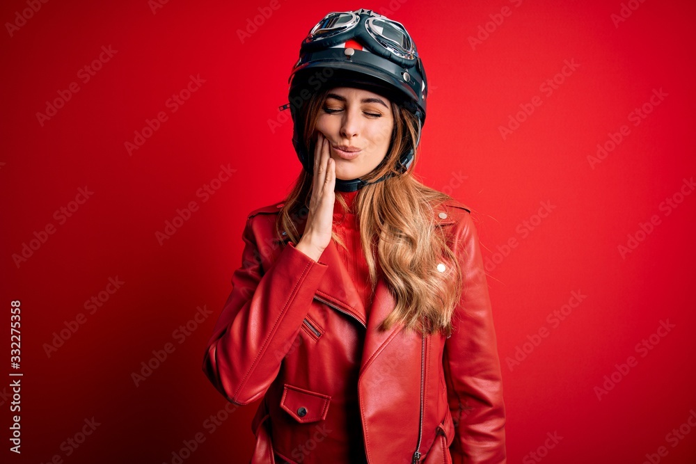 Young beautiful brunette motrocyclist woman wearing moto helmet over red background touching mouth with hand with painful expression because of toothache or dental illness on teeth. Dentist Young beautiful brunette motrocyclist woman wearing moto helmet over red background touching mouth with hand with painful expression because of toothache or dental illness on teeth. Dentist